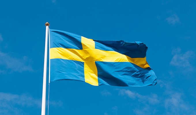 Svenska flaggan är hissad och vajar i vinden mot en klarblå himmel.
