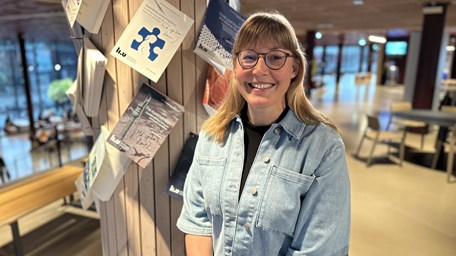 Kvinna i jeansjacka och glasögon står vid en pelare med uppspikade doktorsavhandlingar.