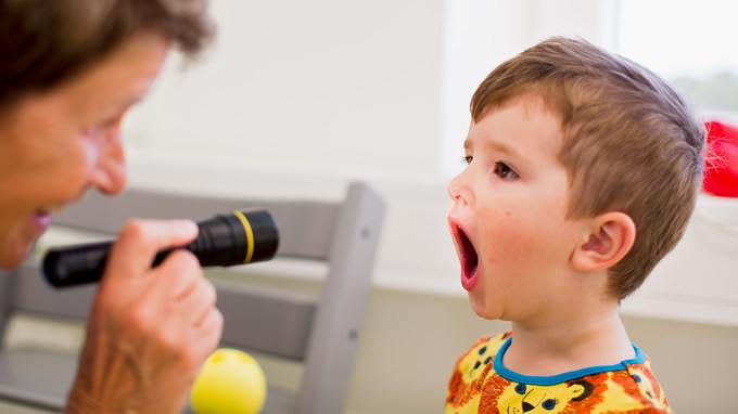 Barnsjuksköterska lyser med ficklampa i treårig pojkes mun och tittar in.