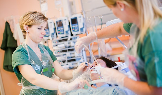 Två kvinnliga sjuksköterskor tränar på att sätta fast slangar för syre på en kollega som spelar patient. I bakgrunden syns maskiner