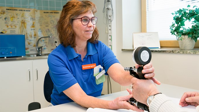 Kvinna i blå vårdkläder undersöker patient med karpaltunnelsyndrom, besvär med domningar och nedsatt kraft i handen. 