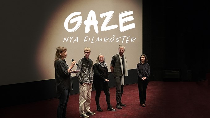 Fem personer står på en scen i en nedsläckt biosalong. På bioduken bakom dem står texten GAZE - nya filmröster. 
