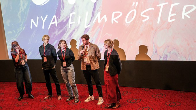 fem människor samtalar framför en bioduk. 