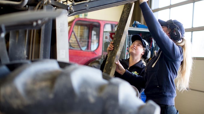 Två tjejer reparerar en traktor. 