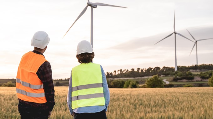 Två människor som samverkar med vindkraftverk i bakgrunden. 
