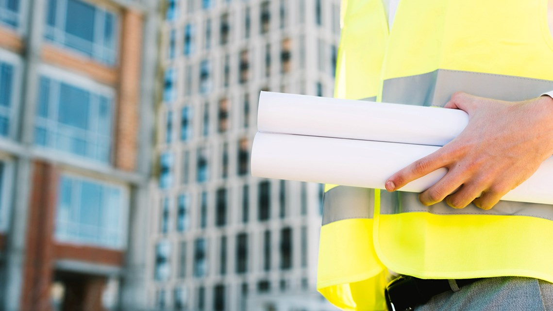 Man i varselväst med byggnader i bakgrunden.