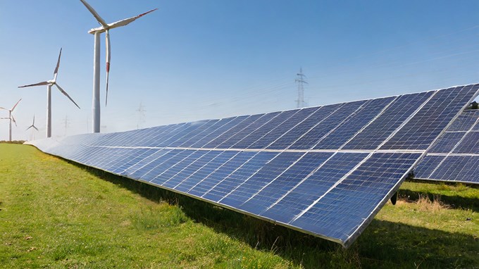 Solceller, vindkraftverk och transmissionsnät på ett grön fält med strålande sol en vacker sommardag.