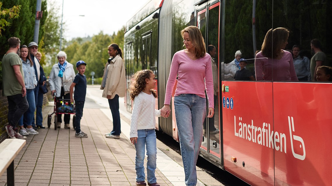 Person håller barn i handen, går längs med bussen. 