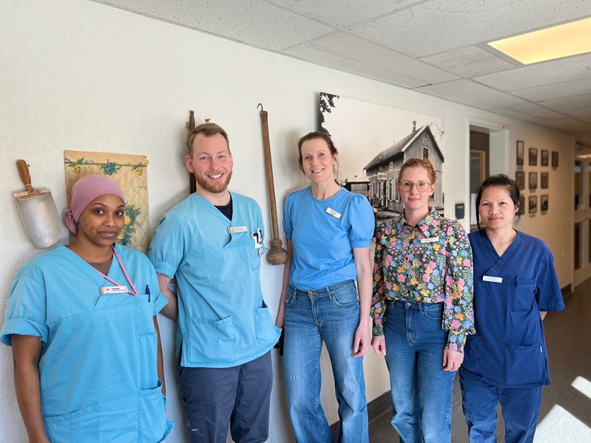 Fem medarbetare på en demensenhet i blåa klinikkläder står bredvid varandra och ler mot kameran.