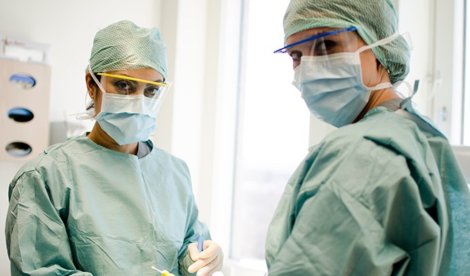 Två tandläkare med munskydd utför ingrepp på patient
