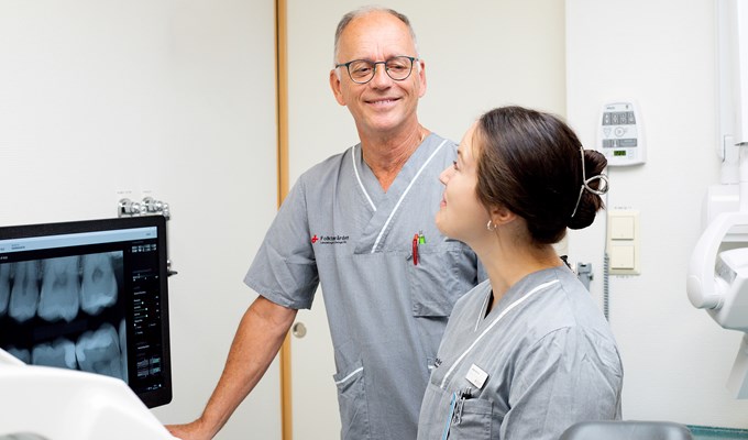 En man och en kvinna tittar på varandra. De står i ett behandlingsrum och är klinikklädda.