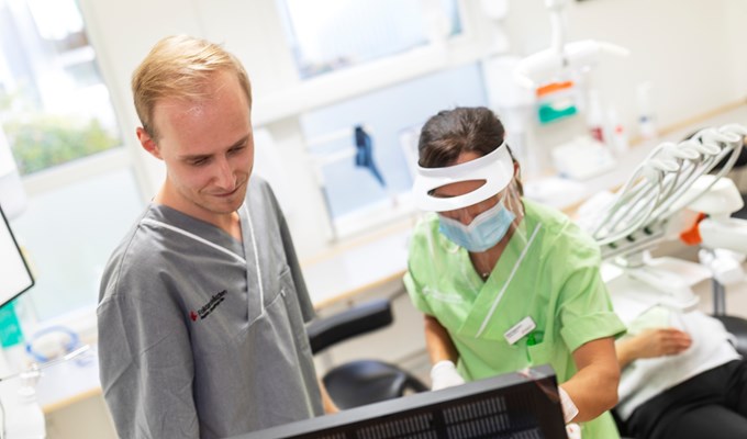 Två tandvårdspersonal står bredvid varandra på en tandvårdsklinik och tittar på en datorskärm. 