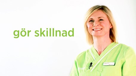 En kvinna i klinikkläder ler in i kameran.
