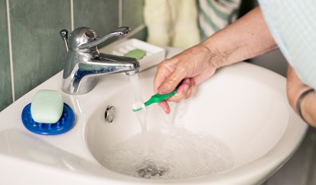 En äldre persons hand håller en tandborste under rinnande vatten