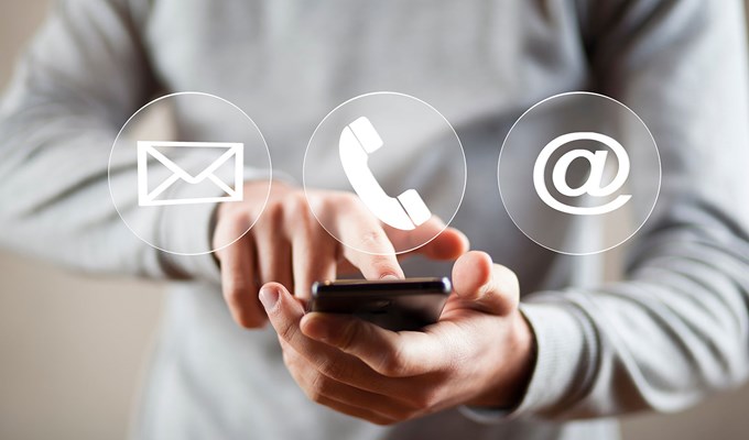 Händer som håller i en mobiltelefon och tre ikoner som föreställer adress, telefon och e-post.