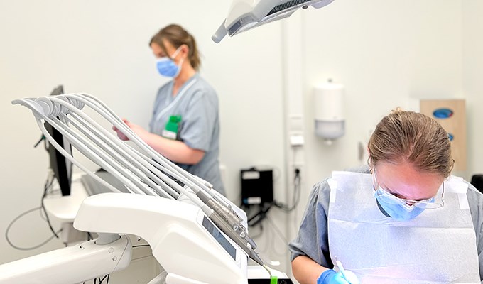 En kvinnlig tandhygienist behandlar en patient som ligger i en behandlingsstol. 