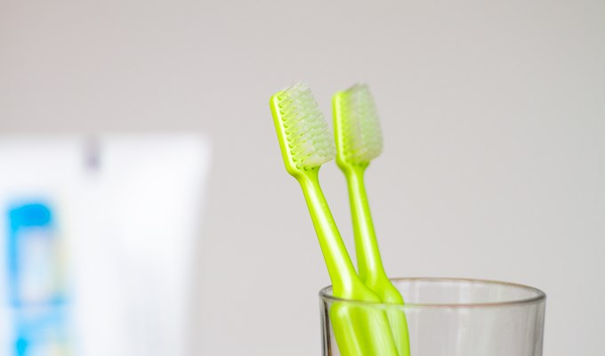 Två gröna tandborstar i ett glas bakom en tandkrämstub
