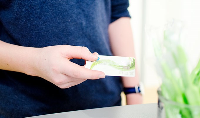 Person håller i ett betalkort framför gröna tandborstar