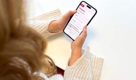 En kvinna håller en mobiltelefon som visar inloggningssidan till 1177.