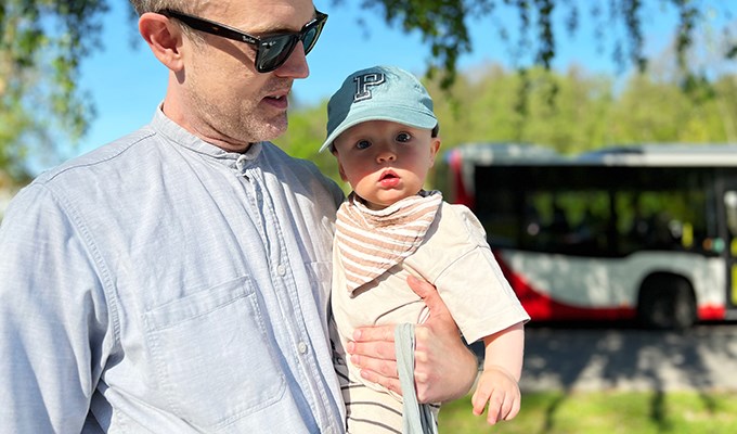 En pappa står utomhus och håller sin 1-åriga son i famnen.