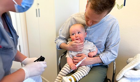 En pappa sitter ner och håller i sin ettåriga son. En tandsköterska är på väg att göra en undersökning på sonen.