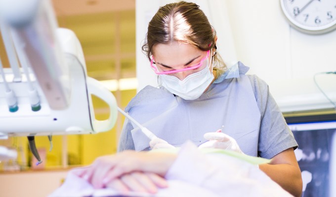 Mörkhårig tjej med munskydd undersöker en patient i behandlingsstol