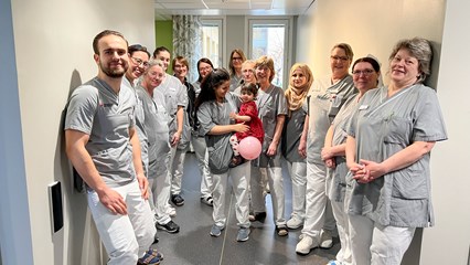 Många glada medarbetare i klinikkläder som står i en korridor.