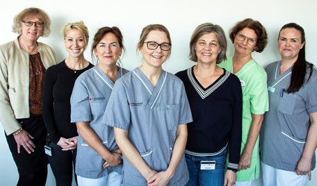 En gruppbild med kvinnor som står på rad och ler in i kameran. De har gröna, svarta, gråa och beige kläder.