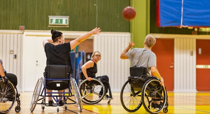 Tre personer i rullstol som spelar basket i en idrottshall
