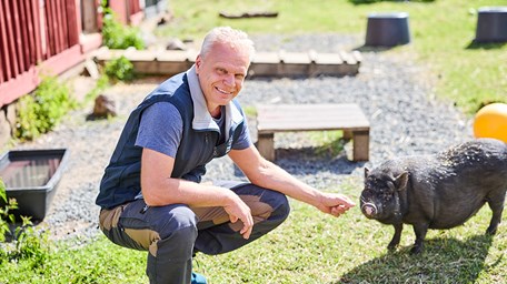 Peron ler mot kameran och klappar en mini-gris.