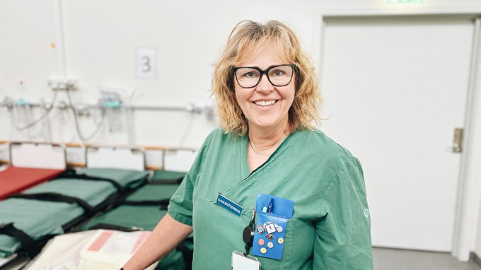 En person ler mot kameran, Hon jobbar på akuten och är klädd i arbetskläder. 