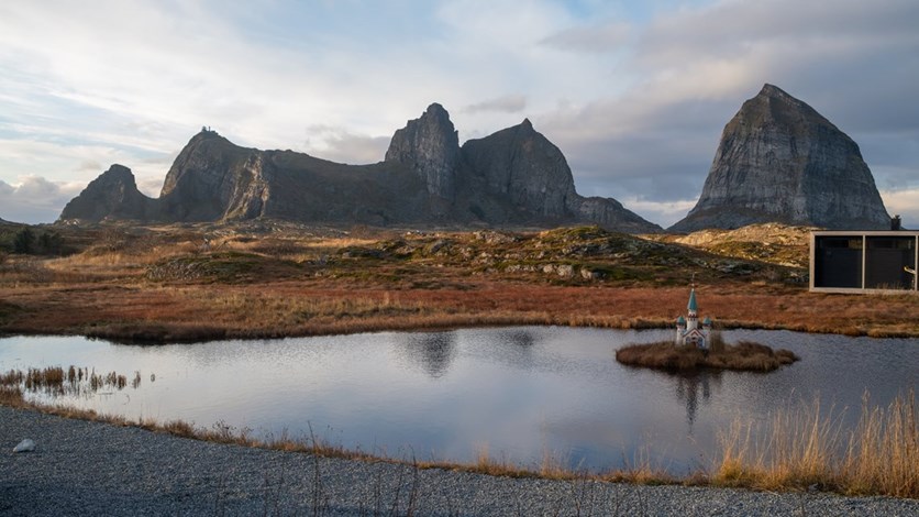 Ett landskap med låga berg i bakgrunden, en liten damm i förgrunden och ett miniatyrhus på en liten ö. 