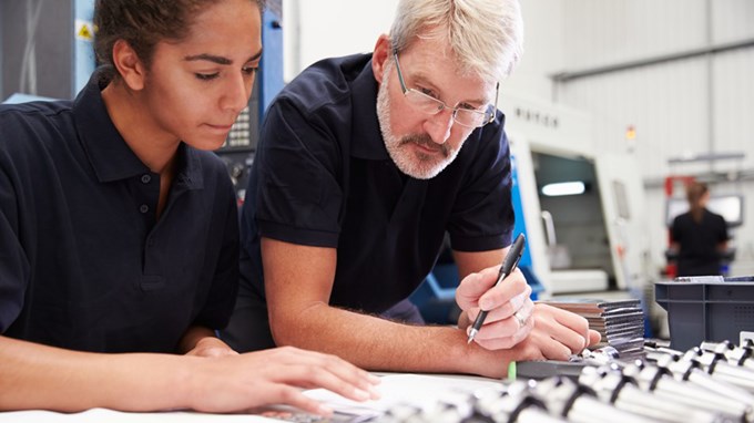 En äldre man och en ung kvinna tittar på några föremål på en industri. 