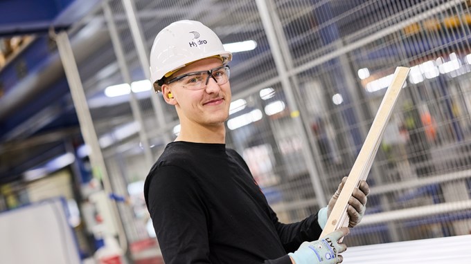 Ung man på industri med hjälm och skyddsglasögon tittar in i kameran och ler. 