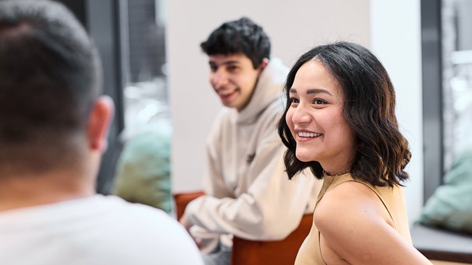En ung kvinna med kort mörkt hår ler och tittar på en man som sitter intill. 