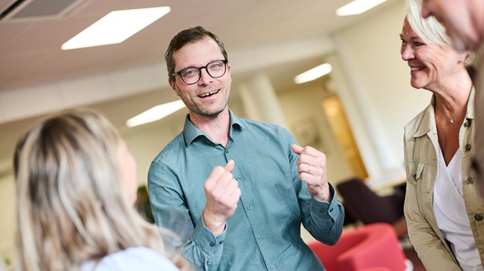 En man med glasögon och skjorta. Tittar in i kameran och ler. 