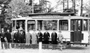En grupp herrar, 14 personer, poserar framför spårvagnen som är på väg till ”Utställningen 1928” på A 6 kasernområde. Spårvagnsföraren syns på sin plats.