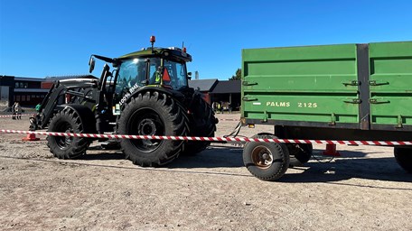 En svart traktor med ett grönt släp