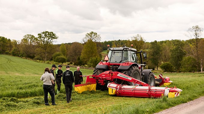 Elever och lärare står på en åker med gräs och en traktor.
