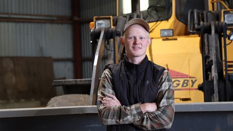 Anton står i maskinhallen framför sin traktor.