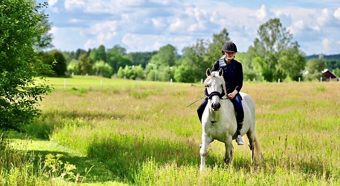 En flicka rider barbacka på sin vita ponny i en grönskande hage