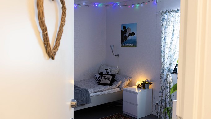 En inblick i ett möblerat elevrum på internatet med säng, sängbord, en matta, kuddar och lampa.