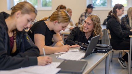 En lärare ler mot två elever som sitter i klassrummet.