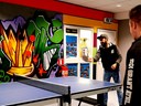 En person spelar pingis. I bakgrunden en färgglad vägg med graffitti.