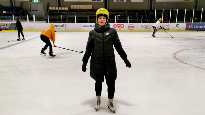 Tjej med gul hjälm och svart vinterjacka åker skridsko i en ishall