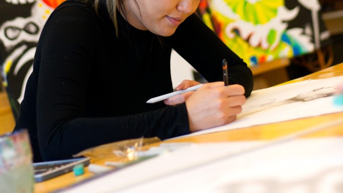 Ung kvinna sitter vid ett bord och håller i en penna som hon använder för att teckna på ett papper.